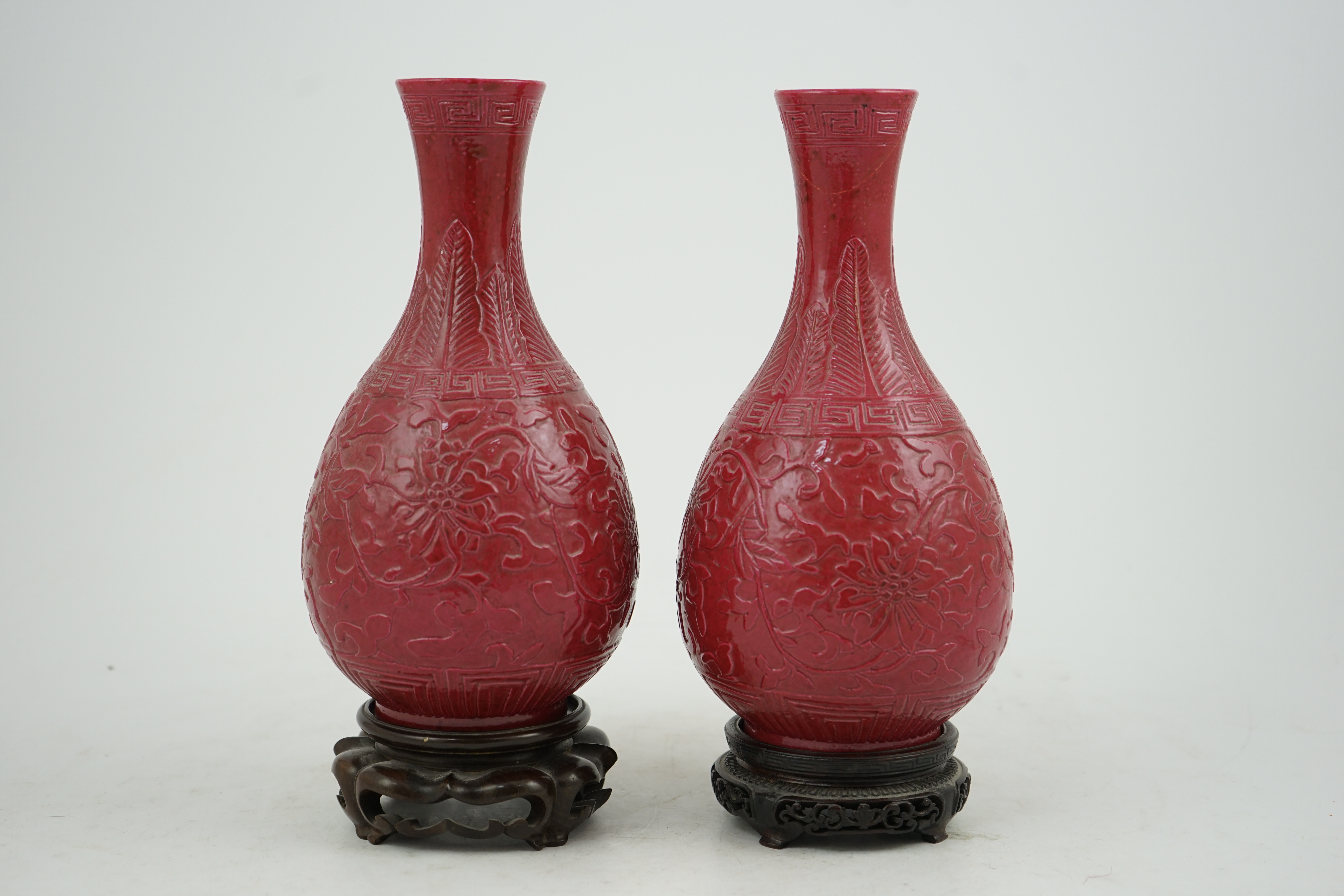 A pair of Chinese ruby ground ‘lotus’ bottle vases, late 19th century, each carved in relief with lotus flowers, scrolling tendrils and leaves, both with carved stands, 24cm high. Condition - one vase the neck broken bot